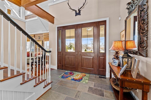 entryway featuring stairs, beamed ceiling, stone tile flooring, and baseboards