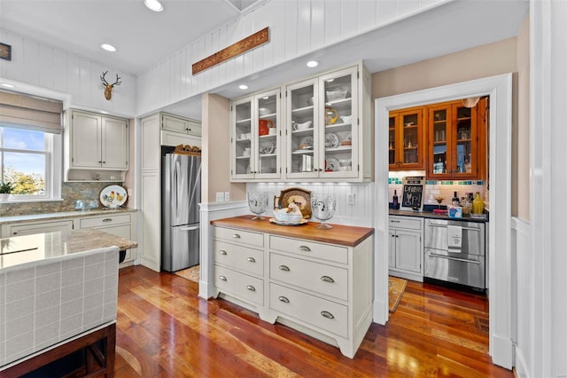 kitchen featuring glass insert cabinets, dark wood finished floors, freestanding refrigerator, and decorative backsplash