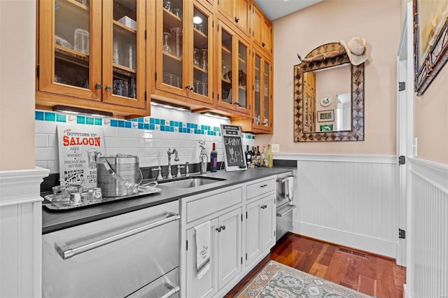 kitchen featuring dark wood-style flooring, a sink, wainscoting, dark countertops, and glass insert cabinets