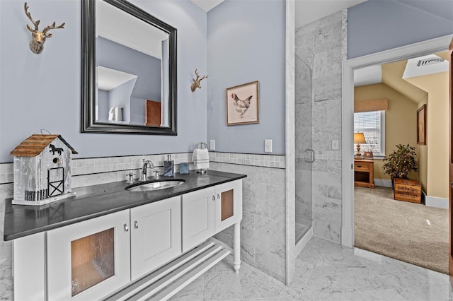 bathroom featuring vanity, tile walls, marble finish floor, wainscoting, and a shower with door