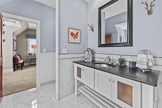 ensuite bathroom featuring lofted ceiling, visible vents, vanity, marble finish floor, and wainscoting