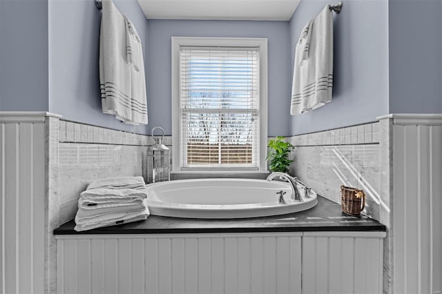 bathroom featuring wainscoting and a bath