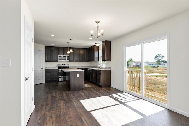 kitchen with appliances with stainless steel finishes, dark hardwood / wood-style flooring, dark brown cabinetry, decorative light fixtures, and a center island