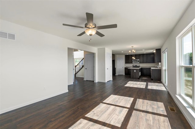 unfurnished living room featuring plenty of natural light, ceiling fan with notable chandelier, dark hardwood / wood-style floors, and sink