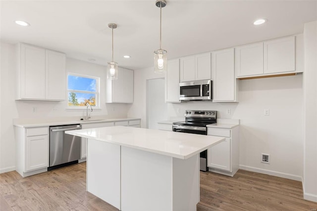 kitchen with white cabinets, light hardwood / wood-style flooring, appliances with stainless steel finishes, decorative light fixtures, and a kitchen island