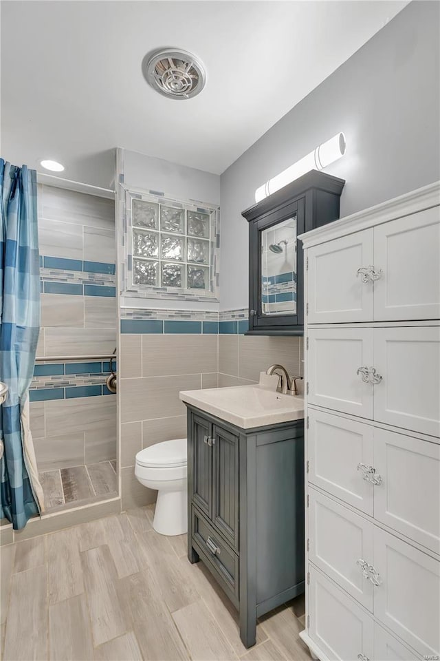 bathroom with curtained shower, vanity, tile walls, and toilet