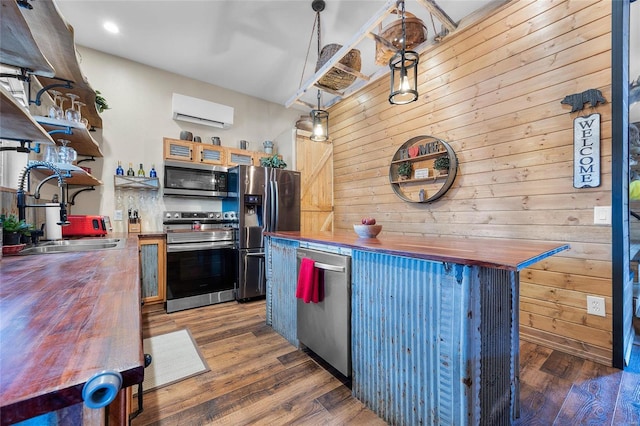 kitchen featuring decorative light fixtures, sink, wooden walls, stainless steel appliances, and wood counters