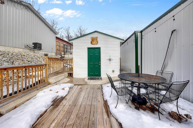 snow covered deck featuring central AC unit and a storage shed