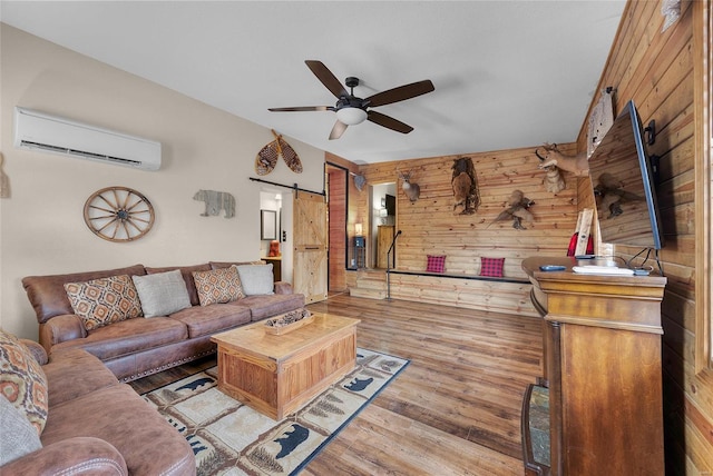 living room with ceiling fan, a barn door, an AC wall unit, wooden walls, and light hardwood / wood-style flooring