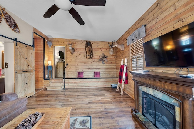 living room with hardwood / wood-style flooring, ceiling fan, a barn door, and wood walls