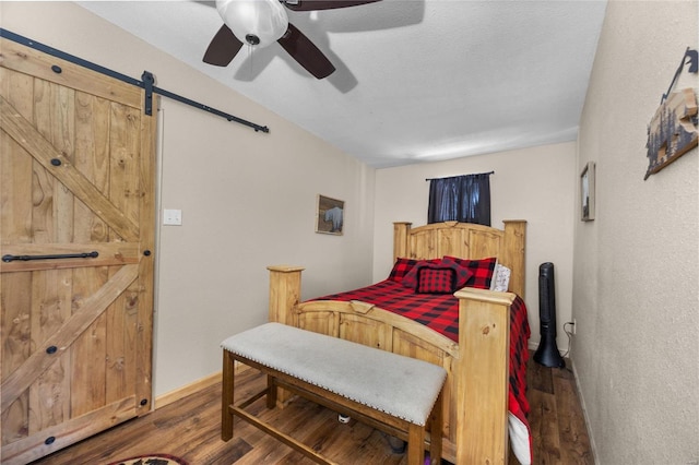 bedroom with ceiling fan, a barn door, and hardwood / wood-style flooring