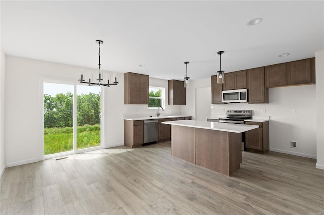 kitchen with hanging light fixtures, light hardwood / wood-style floors, a notable chandelier, a kitchen island, and stainless steel appliances