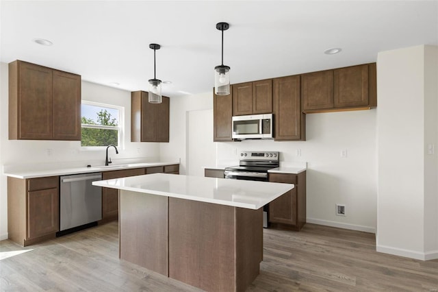 kitchen with appliances with stainless steel finishes, light wood-type flooring, sink, decorative light fixtures, and a kitchen island