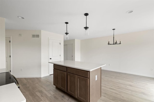 kitchen with an inviting chandelier, a kitchen island, hanging light fixtures, and light hardwood / wood-style floors