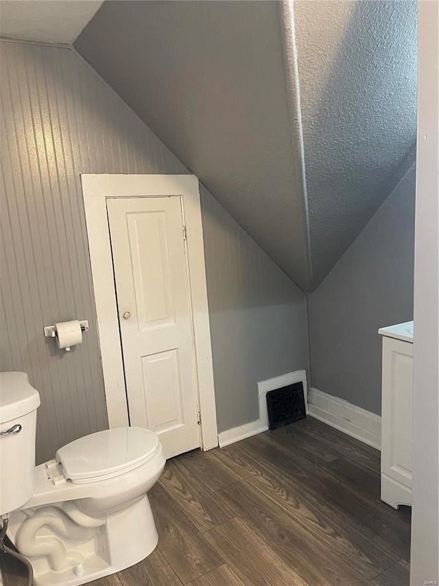 bathroom featuring wood walls, hardwood / wood-style floors, toilet, and vaulted ceiling