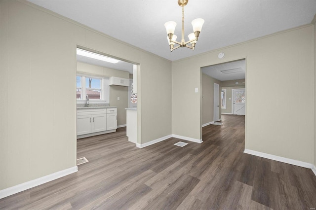 unfurnished dining area featuring dark hardwood / wood-style flooring, crown molding, sink, and an inviting chandelier