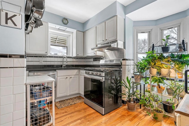 kitchen featuring white cabinetry, sink, stainless steel gas range, light hardwood / wood-style flooring, and backsplash