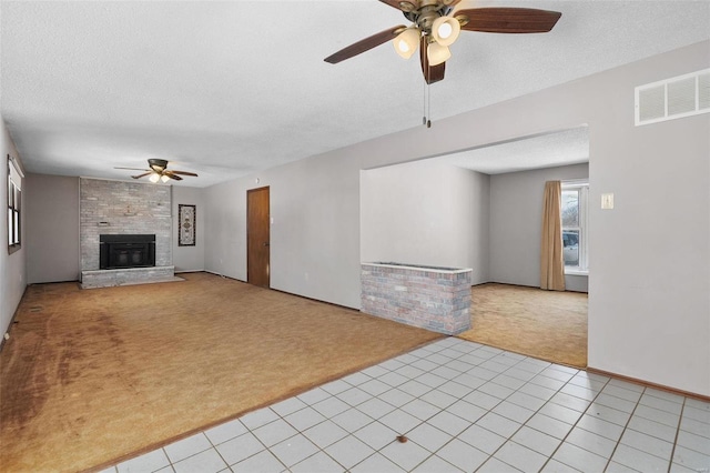 unfurnished living room with a large fireplace, light tile patterned floors, visible vents, light colored carpet, and a textured ceiling