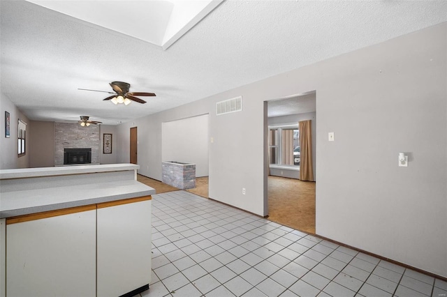 interior space with a skylight, visible vents, ceiling fan, a textured ceiling, and a fireplace