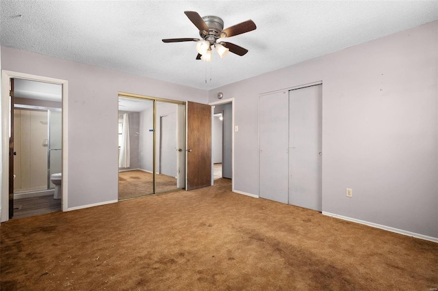 unfurnished bedroom featuring baseboards, ensuite bath, a textured ceiling, carpet flooring, and two closets