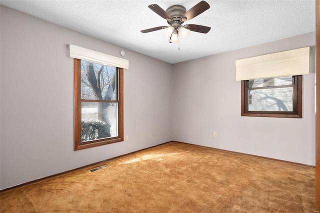 empty room with carpet floors, visible vents, a textured ceiling, and a ceiling fan