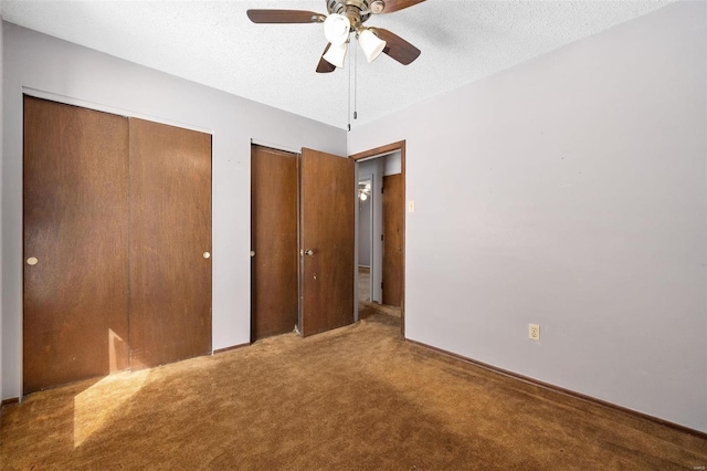 unfurnished bedroom with carpet flooring, ceiling fan, a textured ceiling, and two closets