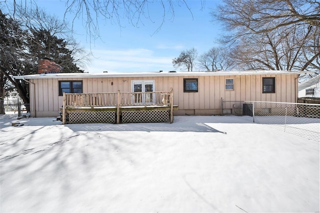 snow covered property featuring board and batten siding, fence, a chimney, and a wooden deck