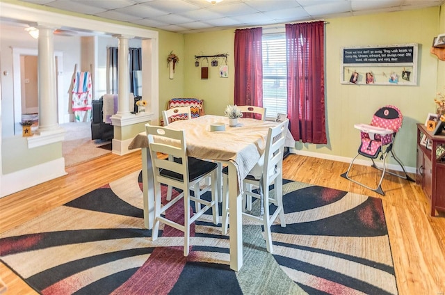 dining space featuring ornate columns, a drop ceiling, and light wood-type flooring