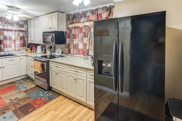 kitchen with light stone counters, light hardwood / wood-style flooring, white cabinets, and black appliances