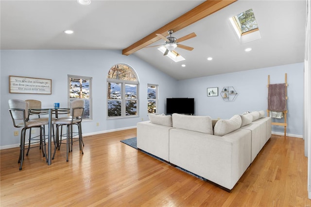 living room with ceiling fan, vaulted ceiling with skylight, and light hardwood / wood-style floors