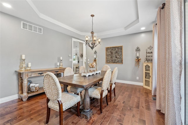 dining area featuring an inviting chandelier, a tray ceiling, and dark wood-type flooring