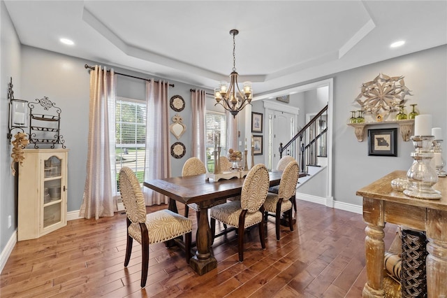 dining area featuring hardwood / wood-style flooring, a raised ceiling, and a notable chandelier