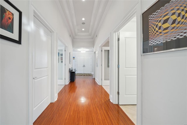 hallway with a raised ceiling, ornamental molding, and light wood-type flooring