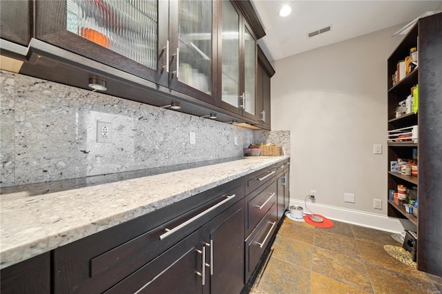 bar with tasteful backsplash, light stone countertops, and dark brown cabinets