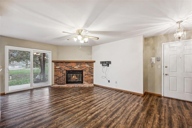 unfurnished living room with ceiling fan with notable chandelier, dark hardwood / wood-style floors, and a brick fireplace