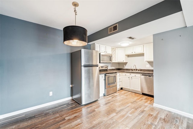 kitchen with appliances with stainless steel finishes, sink, decorative light fixtures, light hardwood / wood-style flooring, and white cabinetry