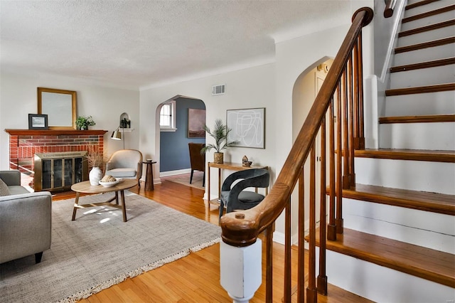 living room featuring wood-type flooring, a brick fireplace, and a textured ceiling