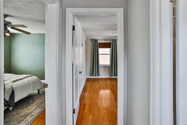 hall with a textured ceiling and light hardwood / wood-style floors