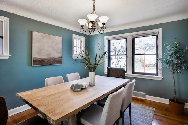 dining space with a textured ceiling, dark hardwood / wood-style floors, and a chandelier