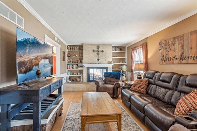 living room featuring a textured ceiling, built in shelves, a fireplace, light hardwood / wood-style flooring, and crown molding