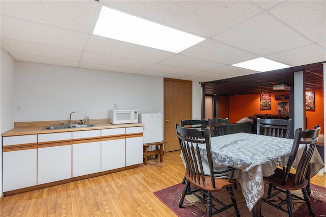 dining room with sink, light hardwood / wood-style flooring, and a paneled ceiling