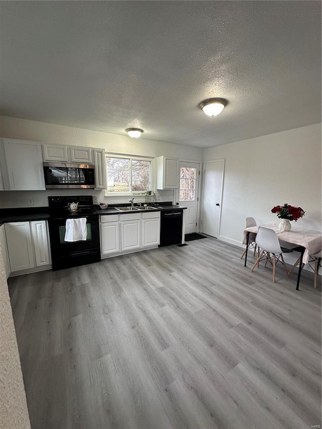 kitchen with sink, black appliances, a textured ceiling, white cabinets, and light wood-type flooring