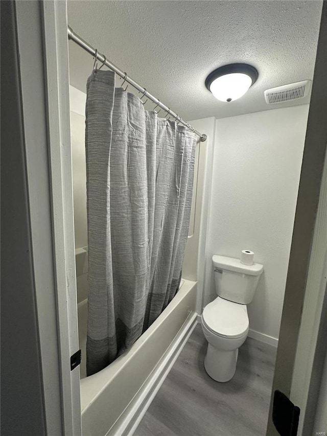 bathroom with shower / bath combo with shower curtain, hardwood / wood-style floors, a textured ceiling, and toilet