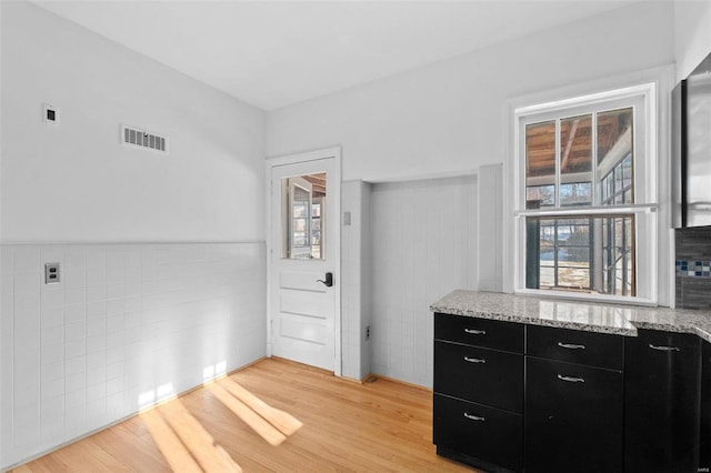 kitchen with tile walls, light stone counters, and light hardwood / wood-style floors