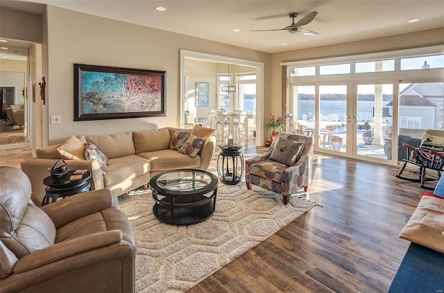 living room featuring ceiling fan, a water view, dark wood-type flooring, and french doors