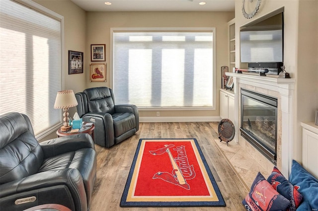 living room featuring light wood-type flooring, built in features, and a tiled fireplace