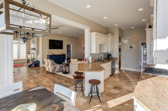 kitchen with sink, stainless steel appliances, light stone counters, a breakfast bar area, and decorative backsplash