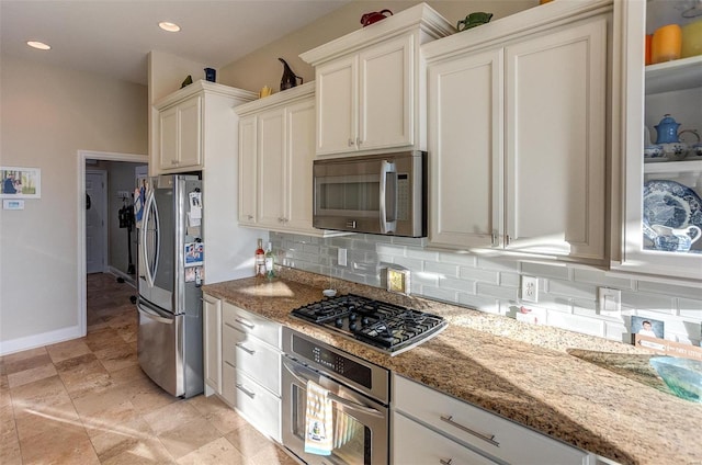 kitchen with stainless steel appliances, white cabinetry, tasteful backsplash, and dark stone counters