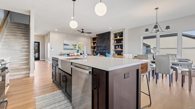 kitchen featuring sink, stainless steel appliances, built in features, an island with sink, and pendant lighting