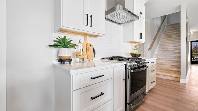 kitchen featuring white cabinets, wall chimney range hood, stainless steel gas stove, light wood-type flooring, and rustic walls